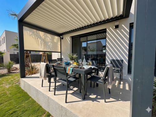 Patio de villa contemporaine avec table à manger, pergola à lames orientables et vue sur le jardin à Conciergerie IB, Canet-en-Roussillon