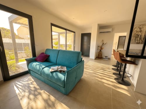 Salon lumineux et moderne avec canapé turquoise, carrelage et vue sur le jardin à Conciergerie IB