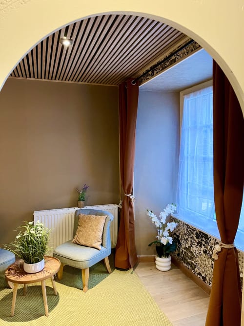 Chambre cosy au Manoir Des Haies avec fauteuil bleu, fleurs en pot, table en bois et vue sur le jardin