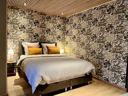 Chambre élégante au Manoir Des Haies avec papier peint à motifs, lit queen-size aux oreillers dorés et vue sur le jardin
