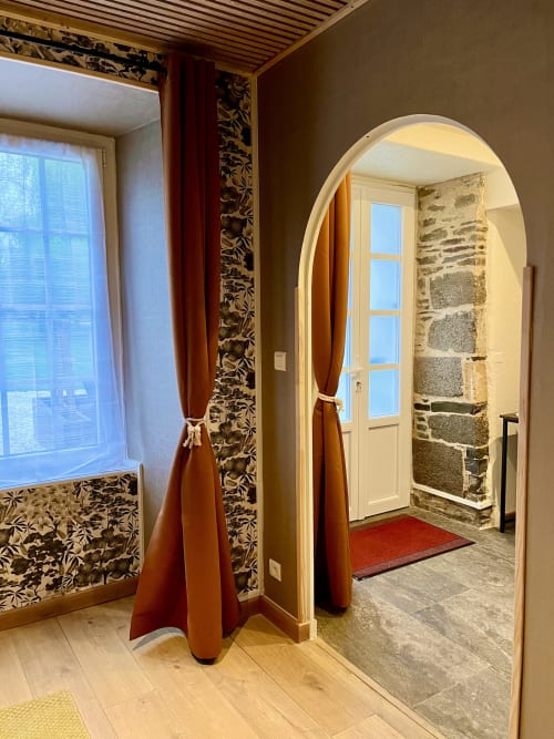 Entrée élégante du Manoir Des Haies avec portail en arche, rideaux rouges et voûte en pierre donnant sur la vue du jardin