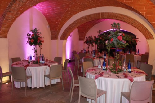 Elegant event venue at Il Casale in Pontedera with pink-lit arches, round tables, floral arrangements, and formal place