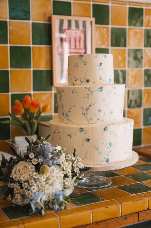 Gâteau de mariage à trois étages avec motifs floraux au Mas de la Vernède, Aramon, aux côtés du bouquet de mariée et d'un fond de carreaux colorés