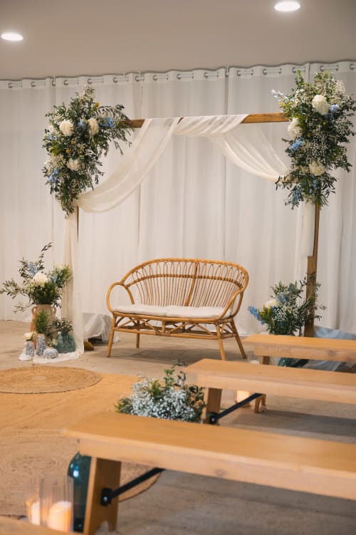 Décoration élégante du lieu de réception au Mas de la Vernède avec chaises tressées, arche florale, bancs en bois et voilage blanc