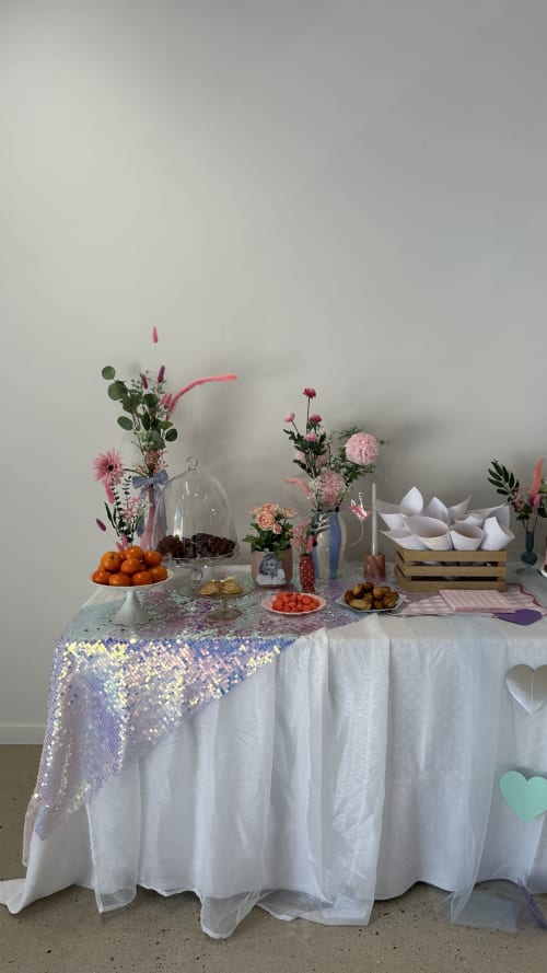Élégante présentation de table au Mas de la Vernède avec fleurs roses, chemin de table à paillettes, fruits frais et linges blancs