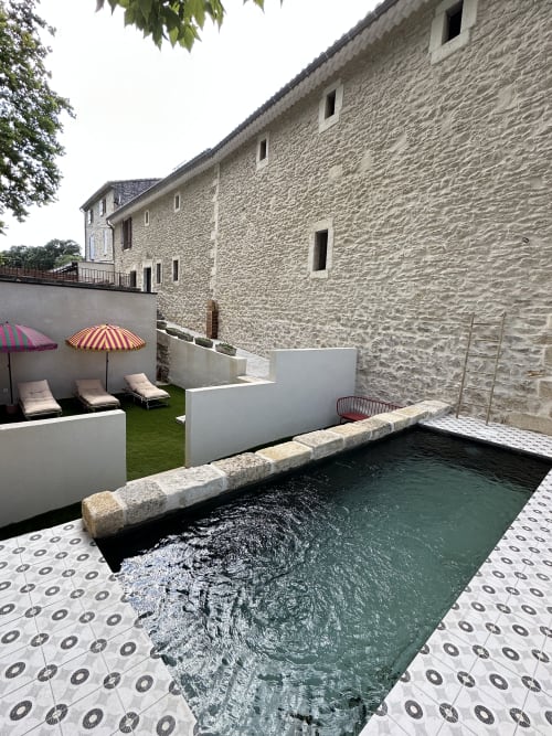 Private pool courtyard at Le Mas de la Vernède cottage in Aramon with loungers, red umbrellas, and stone walls