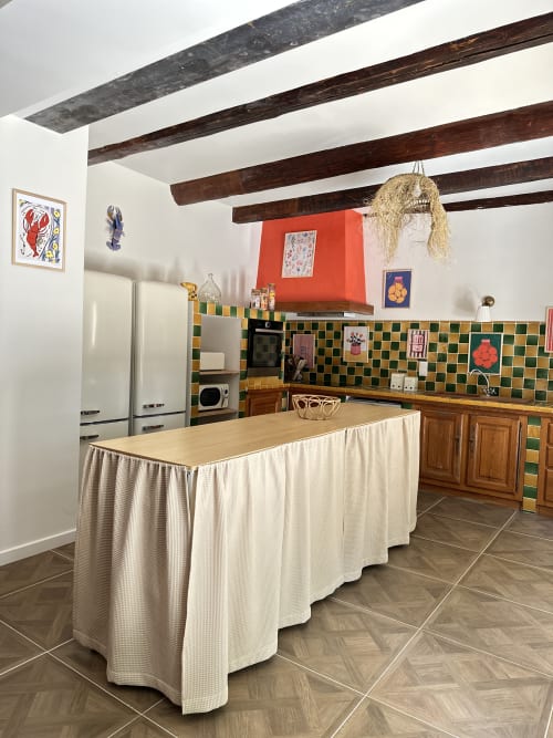 Cottage kitchen with dark beams, green and gold tile backsplash, red accent wall, and island at Le Mas de la Vernède