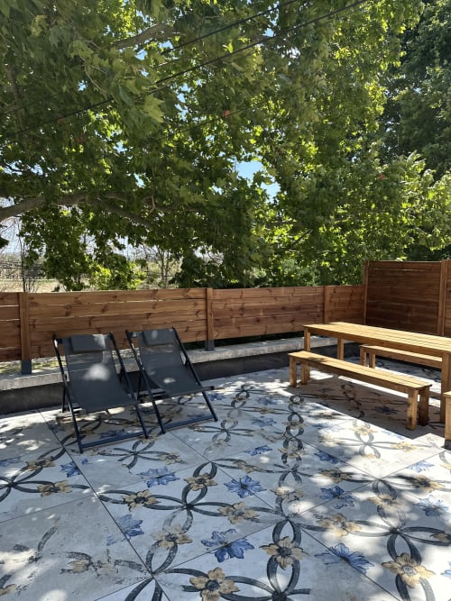 Outdoor patio at Le Mas de la Vernède cottage with lounge chairs, wooden benches, and shade trees in Aramon