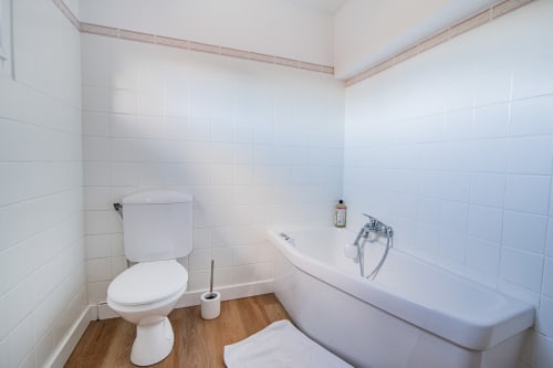 Clean bathroom with white tile walls, toilet, bathtub, and wooden floor at Bise de la Jouvence apartment in Saint Laurent sur