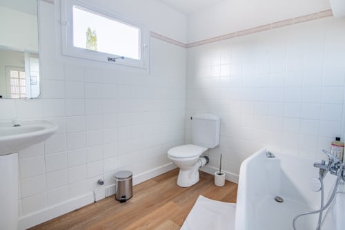 Modern bathroom with white tile walls, wooden floor, toilet, bathtub and sink at Bise de la Jouvence apartment near Puy du