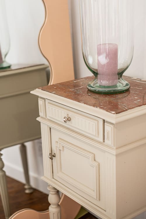 Cream nightstand with marble top and pink candle in glass holder at Bise de la Jouvence B&B