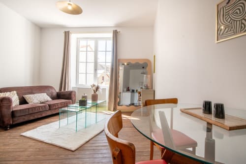 Bright apartment living area with burgundy sofa, glass dining table, wooden chairs, and city views near Puy du Fou in Saint