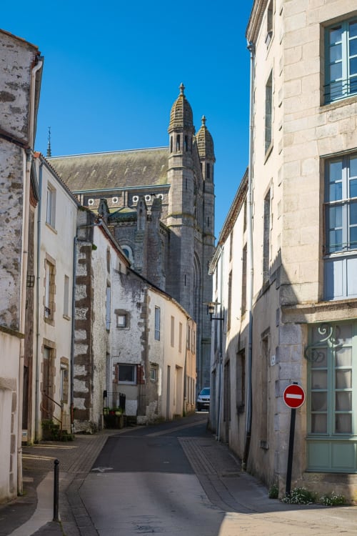 Charmante rue pavée à Saint Laurent sur Sèvre menant à l'église historique aux flèches dorées, illustrant le charme de la ville