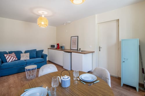 Studio moderne à Bise de la Jouvence avec canapé bleu, table à manger et kitchenette près du Puy du Fou