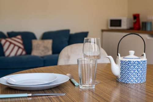 Table dressée à la Bise de la Jouvence avec théière bleue, verre d'eau, assiettes blanches et intérieur d'appartement moderne