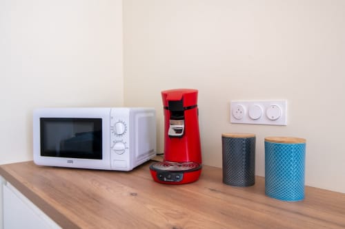 Kitchenette du studio Bise de la Jouvence avec micro-ondes, cafetière rouge et bacs de rangement sur plan de travail en bois