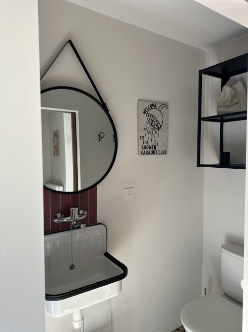 Modern bathroom at Le Mas de la Vernède with circular mirror, sink, toilet, and shower karaoke club sign