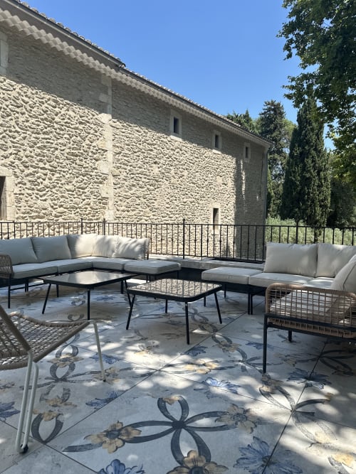 Outdoor terrace at Le Mas de la Vernède with lounge seating, stone buildings, cypress trees, and patterned tiles in Aramon,