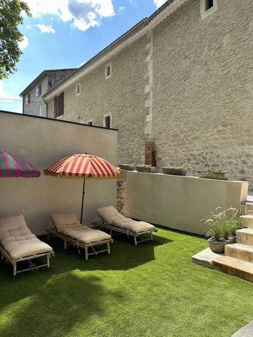 Outdoor terrace at Le Mas de la Vernède with lounge chairs, striped umbrellas, and stone cottage backdrop in Aramon
