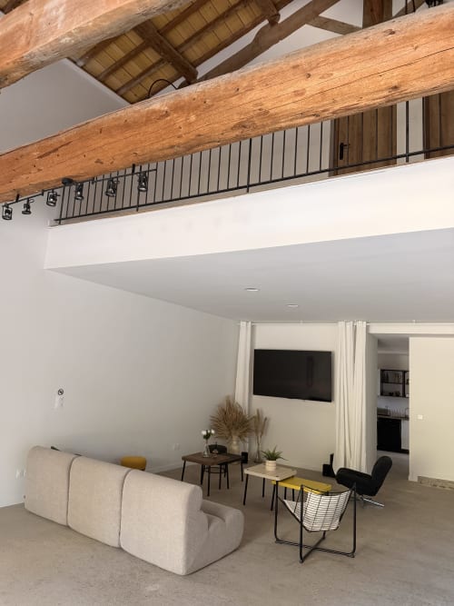 Modern loft-style room at Le Mas de la Vernède with exposed wooden beams, mezzanine, cream sofa, and wall-mounted TV in