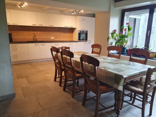Cuisine-salle à manger moderne au gîte Sur La Rive Vierre à Chiny avec table en bois, armoires crème et vue sur le jardin.