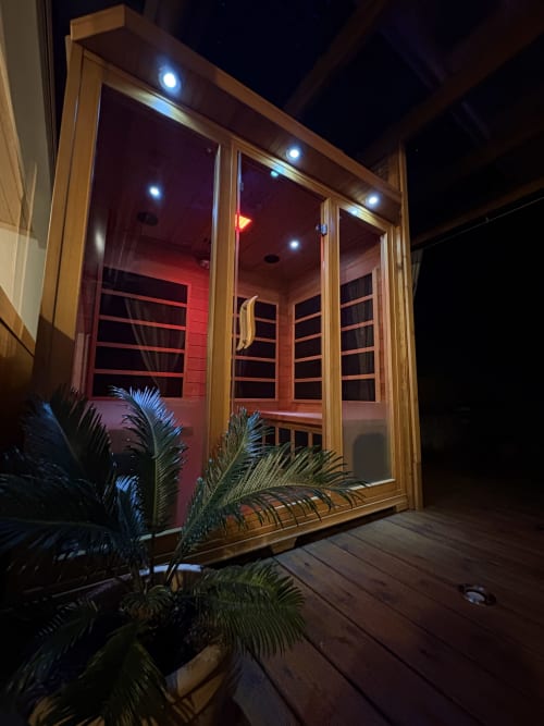 Entrée du luxueux sauna La Kaz 57 la nuit, structure en bois avec éclairage intérieur rouge, La Plaine des Palmistes