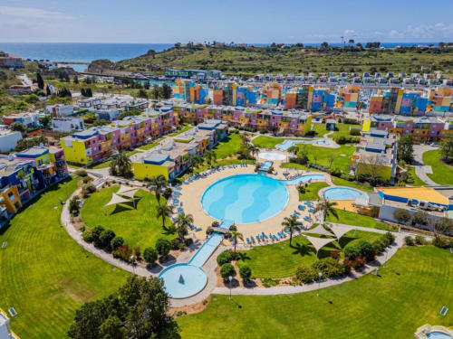 Vista aérea do resort Atlantic Places em Albufeira com apartamentos coloridos, piscinas, jardins e paisagem costeira