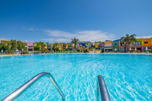 Piscina em turquesa brilhante no Atlantic Places em Albufeira com apartamentos coloridos à beira-mar e palmeiras sob céu azul