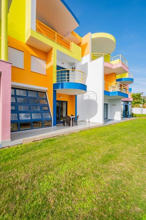 Edifício residencial moderno e colorido em Atlantic Places, Albufeira, com fachada azul e amarela, varandas curvas e jardins