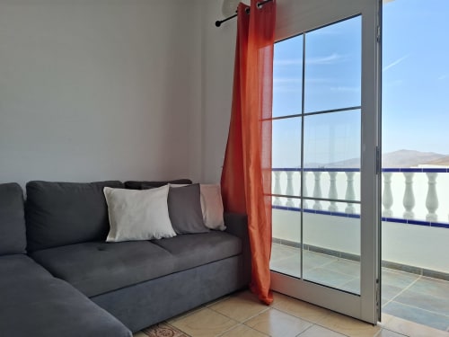 Modern living room with dark sofa, red sheer curtains, and sea view balcony at Villas del Mar in Puerto Calero