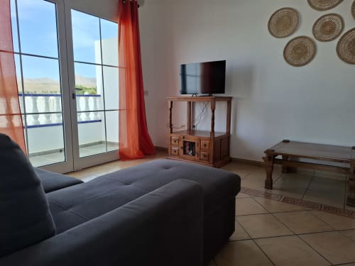 Modern villa living room with sea view, dark sofa, TV, wooden furniture, and ocean panorama through glass doors at Puerto