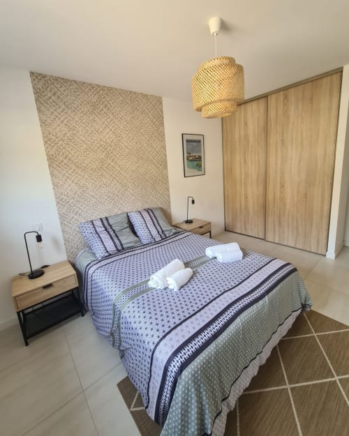 Modern bedroom at Villa Corsica, featuring blue patterned bedding, a woven pendant lamp and wooden accents, managed by the Corsu di Core concierge service.