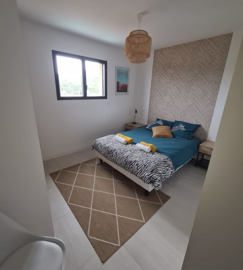 Modern bedroom at Villa Corsica in Favone, featuring blue bedding, a zebra-pattern rug and a rattan pendant light, managed by the Corsu di Core concierge service.