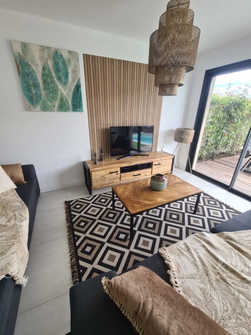 Modern living room of Villa Corsica featuring wooden furniture, a geometric rug, a woven pendant lamp and a view of the pool, managed by the Corsu di Core concierge service.