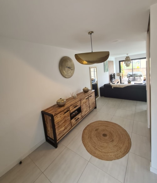 Contemporary villa entrance featuring a wooden sideboard, a brass pendant light, a round jute rug and a wall clock, managed by the Corsu di Core concierge service.