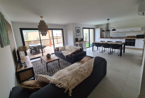 Modern villa living room with black sofas, an open kitchen and direct access to the terrace at Villa Corsica, managed by the Corsu di Core concierge service.