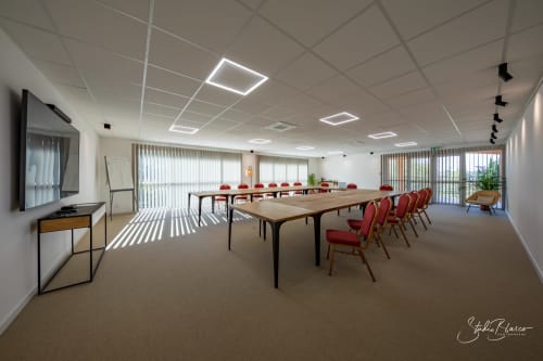 Salle de conférence moderne à l'Hôtel Moulin de la Roque à Althen-des-Paluds avec tables en bois, chaises rouges et lumière naturelle