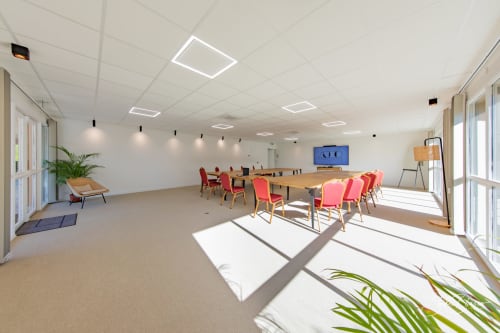Salle de conférence moderne et lumineuse à l'Hôtel Moulin de la Roque avec tables en bois, chaises rouges et lumière naturelle