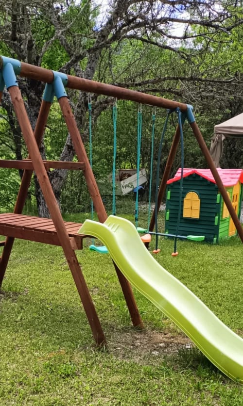 Aire de jeux colorée au Domaine de la Méouge avec toboggan, balançoires et maisonnette entourés d'arbres