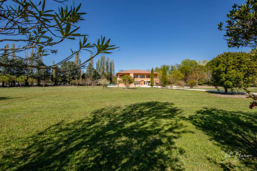 Hôtel Moulin de la Roque à Althen-des-Paluds avec bâtiment en terre cuite, espaces verts et arbres sous ciel bleu