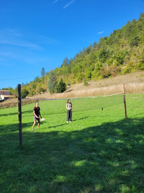 Deux personnes jouent au frisbee dans un champ herbeux aux collines boisées du Domaine de la Méouge, Barret-sur-Méouge