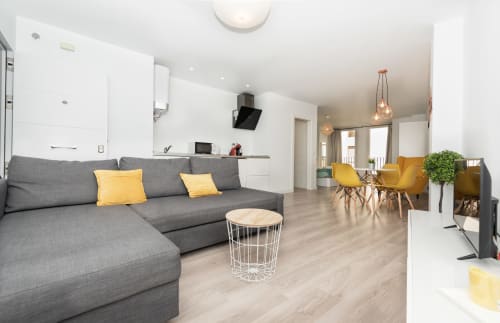 Sur Suites Málaga's Fantástico Loft Amarillo features gray sectional sofa with yellow accents, open kitchen, and dining area.