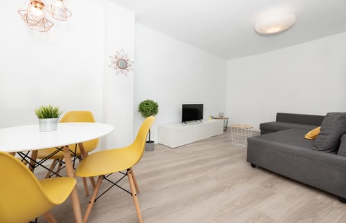 Modern loft at Sur Suites Málaga with yellow chairs, white dining table, gray sofa, TV, and geometric ceiling lights