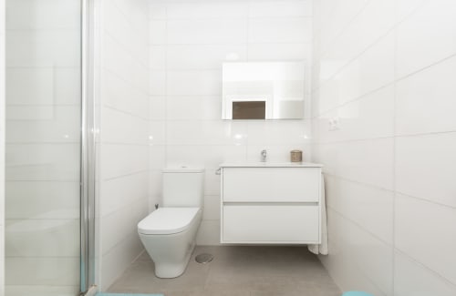 Modern white bathroom at Sur Suites Málaga with toilet, wall-mounted sink vanity, and mirror