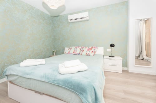 Modern bedroom at Sur Suites Málaga with turquoise patterned wallpaper, light blue bedding, and white furnishings