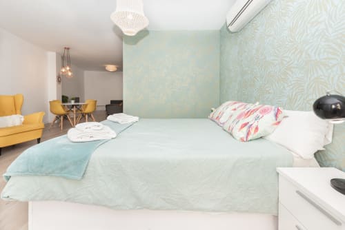 Modern bedroom at Sur Suites Málaga with bed, yellow chair, and turquoise patterned walls