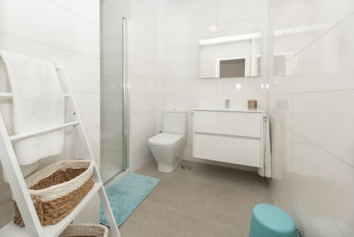 Modern bathroom at Sur Suites Málaga with white tiles, vanity sink, toilet, shower, and coastal turquoise accents