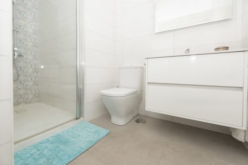 Modern bathroom at Sur Suites Málaga with walk-in shower, white vanity, toilet, and blue bath mat