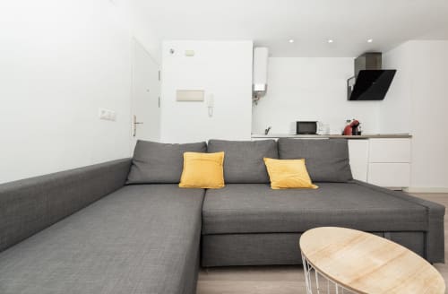 Gray L-shaped sofa with yellow pillows in Sur Suites Málaga loft, kitchen visible behind
