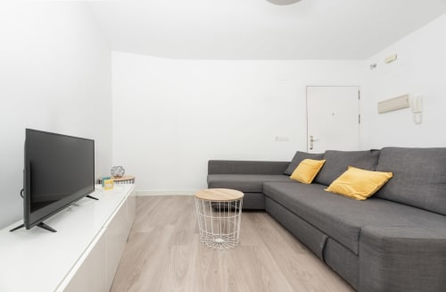 Modern loft living room at Sur Suites Málaga with gray sofa, yellow pillows, TV, and wooden flooring
